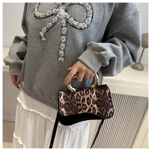Detail of leopard print handbag featuring a unique heart-shaped gold metal top handle
