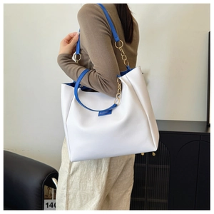 Detail view of white tote bag with blue strap and gold chain accent on shoulder