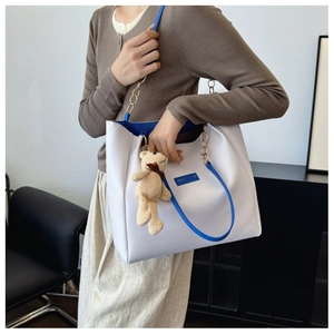 White tote bag with blue trim, chain strap, and cute bear pendant shown on model