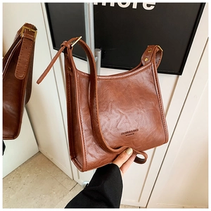 Detail of a brown leather handbag with adjustable gold buckle and embossed text logo