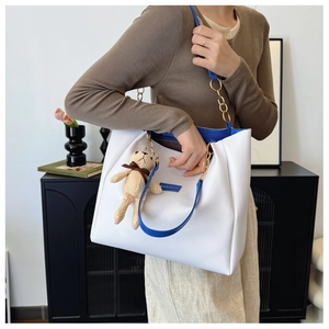 White minimalist leather tote bag with blue straps and brown bear charm on model