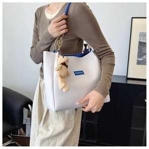 Detail of white tote bag with blue chain strap, fashion label, and cute bear charm