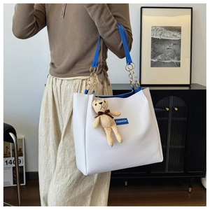 Detail of white tote bag with blue straps, gold chain and knitted bear charm accessory