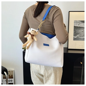 Minimalist white tote bag with blue straps and brown bear charm in a lifestyle interior