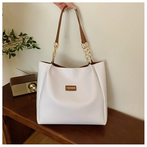 Detail of white tote bag with brown fashion patch and gold chain strap on a bench