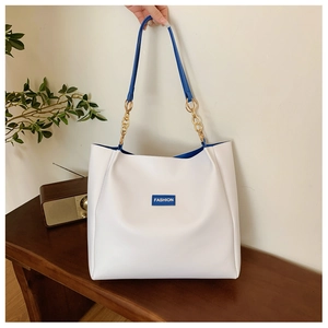 Close-up of a white tote bag with blue interior, gold chain strap, and Fashion label detail