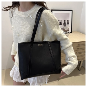 Detail of black pebbled leather tote bag featuring gold New York logo on shoulder strap