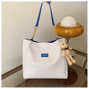 Minimalist white leather tote bag with blue trim, fashion label and gold chain handles