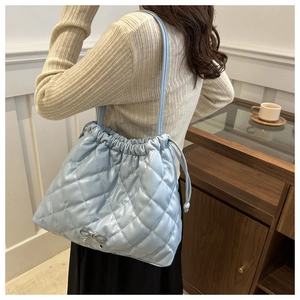 Detail of light blue quilted drawstring bag with a metal bow accent on model