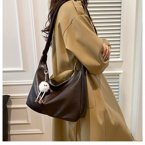 Detail of dark brown faux leather hobo bag with a white plush charm on a trench coat