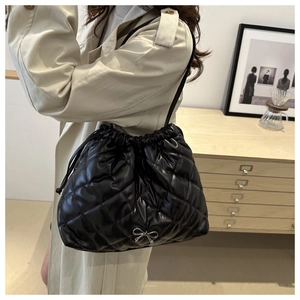 Detail of black quilted drawstring bucket bag with a small silver metal bow ornament