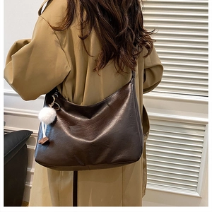 Detail of dark brown faux leather hobo bag with white plush ball charm on a tan trench coat