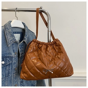 Close-up of brown quilted tote bag with silver bow accent and drawstring closure