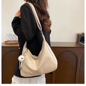 Detailed view of cream PU leather hobo bag with a plush charm on a side-wearing model