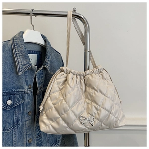 Close-up of cream quilted tote bag featuring silver metal bow and drawstring closure