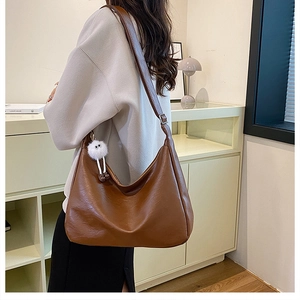 Brown moon-shaped large hobo shoulder bag with fuzzy charm on a model in a cozy room