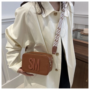 Sac bandoulière marron avec lettres SM embossées et large bandoulière géométrique