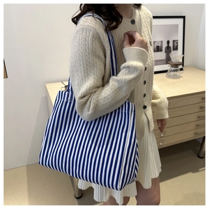 Détail d'un grand sac cabas en toile à rayures bleues et blanches porté par un mannequin