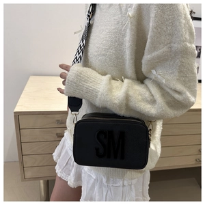 Détail du sac bandoulière noir avec logo SM et large bandoulière à motif géométrique