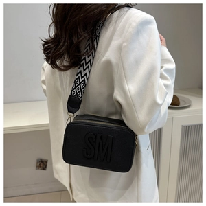Sac bandoulière noir chic avec logo SM et large sangle à motifs sur costume blanc