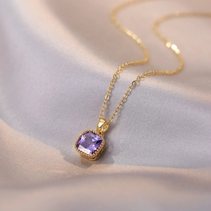Élégant collier doré avec pendentif carré en zircon violet sur un tissu en soie