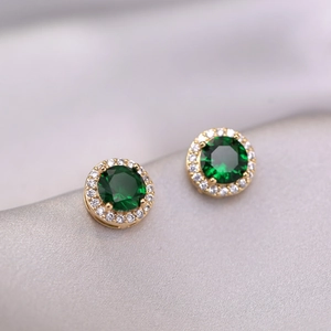 Elegant gold earrings with emerald green zircon halo stones on grey satin background