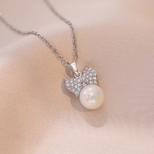 Collier élégant avec pendentif nœud, zircons et perle irisée sur fond de soie