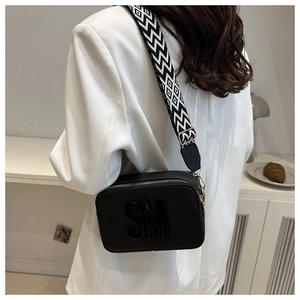 Détail du sac bandoulière noir avec logo SM et large bandoulière tissée à motif géométrique