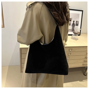 Detail of minimalist black suede hobo bag shown worn on shoulder in a lifestyle setting