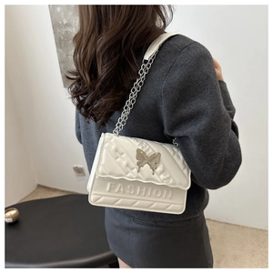 Detailed view of white quilted chain bag featuring a silver butterfly buckle and FASHION text