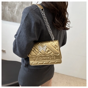 Detail of gold quilted crossbody bag with metal butterfly clasp and chain strap