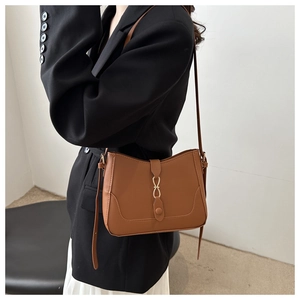 Close-up of brown faux leather shoulder bag featuring a gold metal buckle on a model