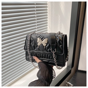 Detail of black quilted crossbody bag featuring silver butterfly buckle and chain strap
