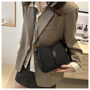 Detail of a black leather shoulder bag featuring a gold infinity buckle on the flap