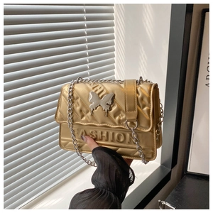 Detail of gold quilted flap bag featuring silver bow charm and Fashion embossed text