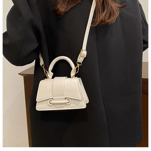 Creamy white textured leather mini handbag with gold hardware worn on a black blazer