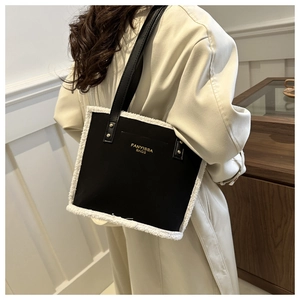 Detail of black tote bag with white faux shearling trim and golden brand logo