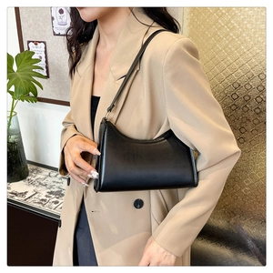 Close-up of a minimalist black half-moon shoulder bag worn with a beige blazer jacket