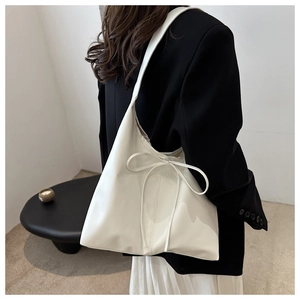 Detail of cream-white leather tote bag with bow knot decoration shown on shoulder