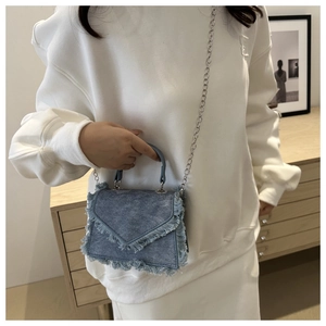 Blue denim crossbody bag with fringe trim and silver chain strap shown on a model