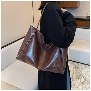 Détail du sac cabas brillant marron foncé en cuir ciré porté avec un blazer noir