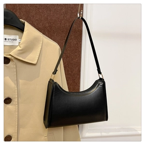 Detail of a chic black leather underarm bag with gold metal buckle next to a trench coat