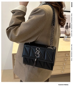 Detail of black quilted crossbody bag with silver SS logo and metallic chain tassel