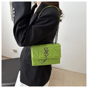 Detail of bright green crossbody bag featuring S-shaped logo with metal tassel and chain