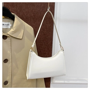 Minimalist white faux leather baguette bag with gold hardware shown on a display rack