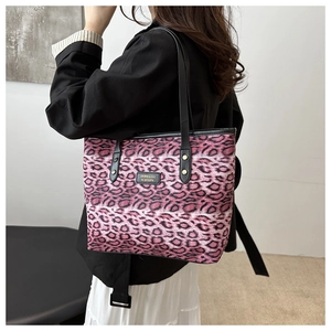 Detail of purple leopard print tote bag with black shoulder straps and metal logo plate