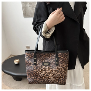 Detail of leopard print tote bag with black leather handles and logo patch