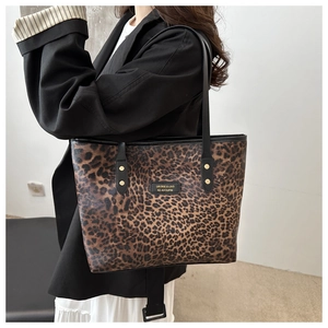 Detail of leopard print tote bag with black leather logo plate and gold metal rivets