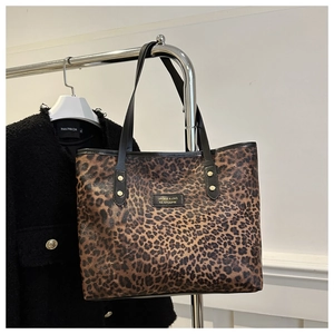 Detail der Tragetasche mit Leopardenmuster, Goldplakette und schwarzen Trageriemen