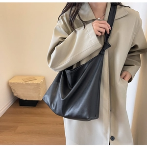Detail of the soft black leather tote bag with unique knotted strap on a khaki trench coat